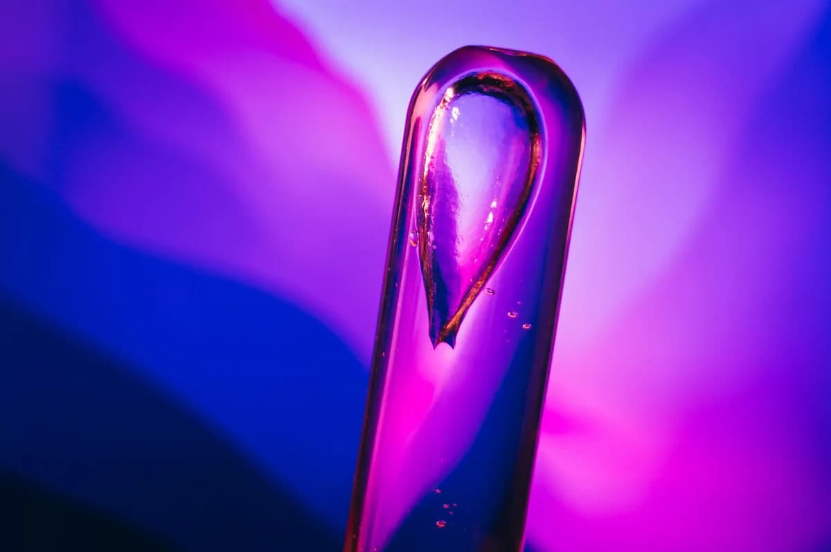 Abstract close-up of a dropper filled with liquid, showcased against a vibrant, colorful background with purple hues.