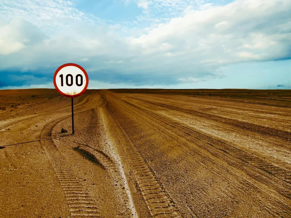 Expansive desert road with a visible 100 speed limit sign and cloudy sky.