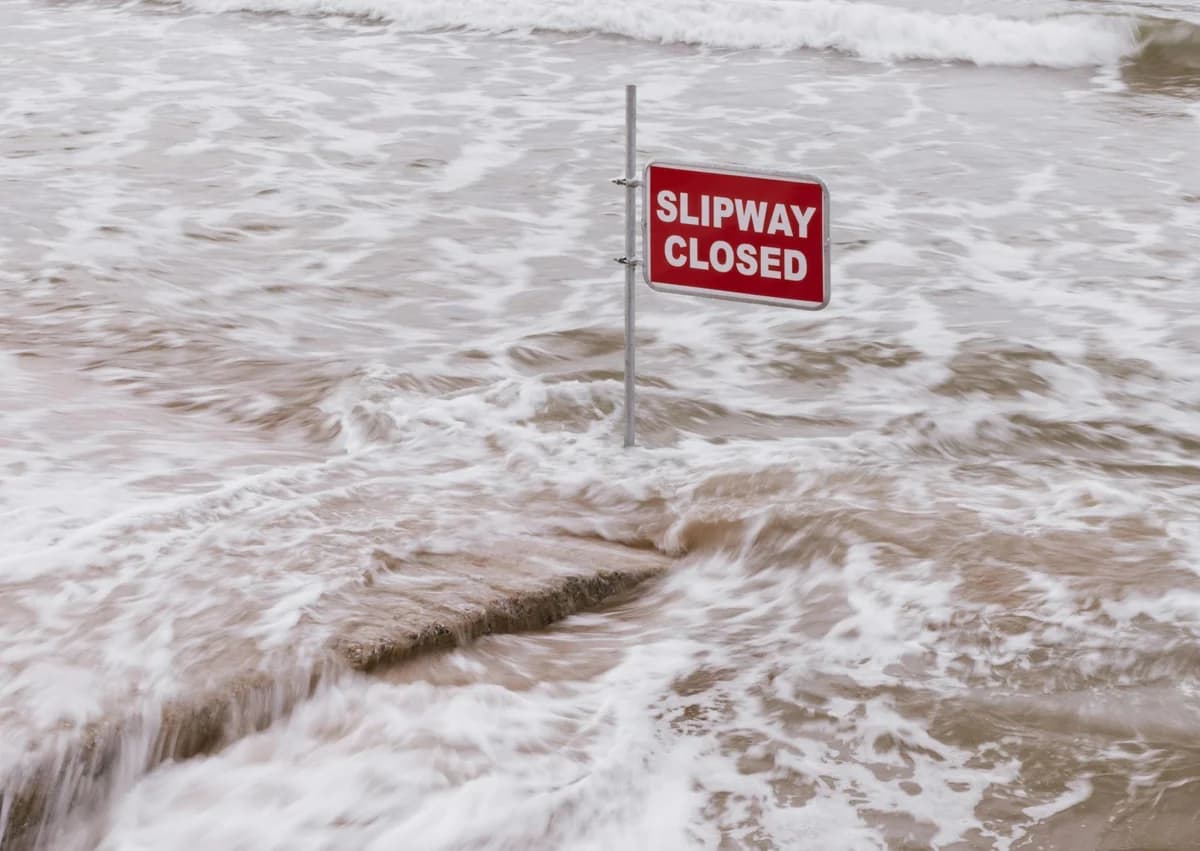 Flooded slipway with red 'Slipway Closed' sign surrounded by flowing waves.