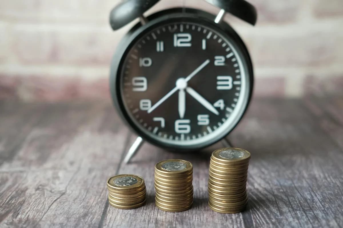 A close-up of an adult's hand dropping a coin into a piggy bank, symbolizing savings and investment.