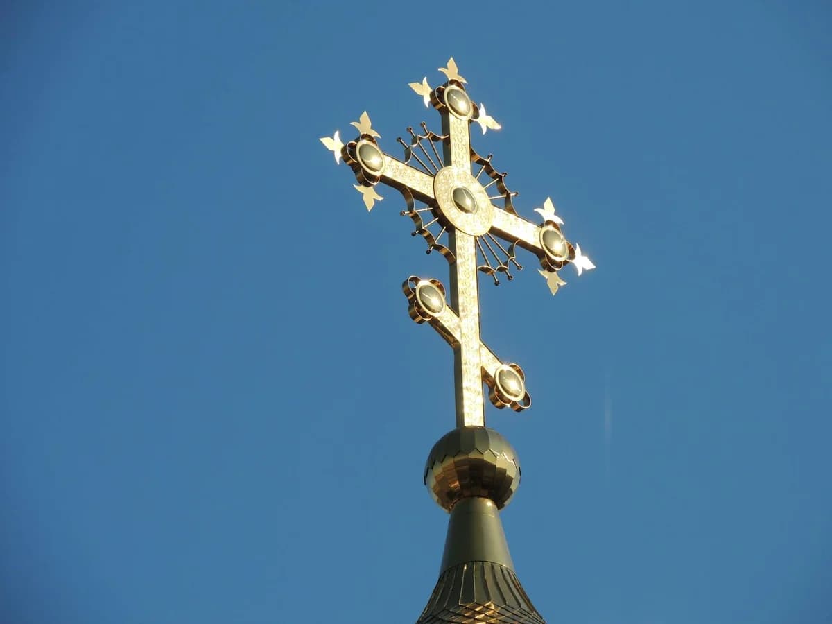 A detailed low angle shot of a golden church cross set against a clear blue sky.