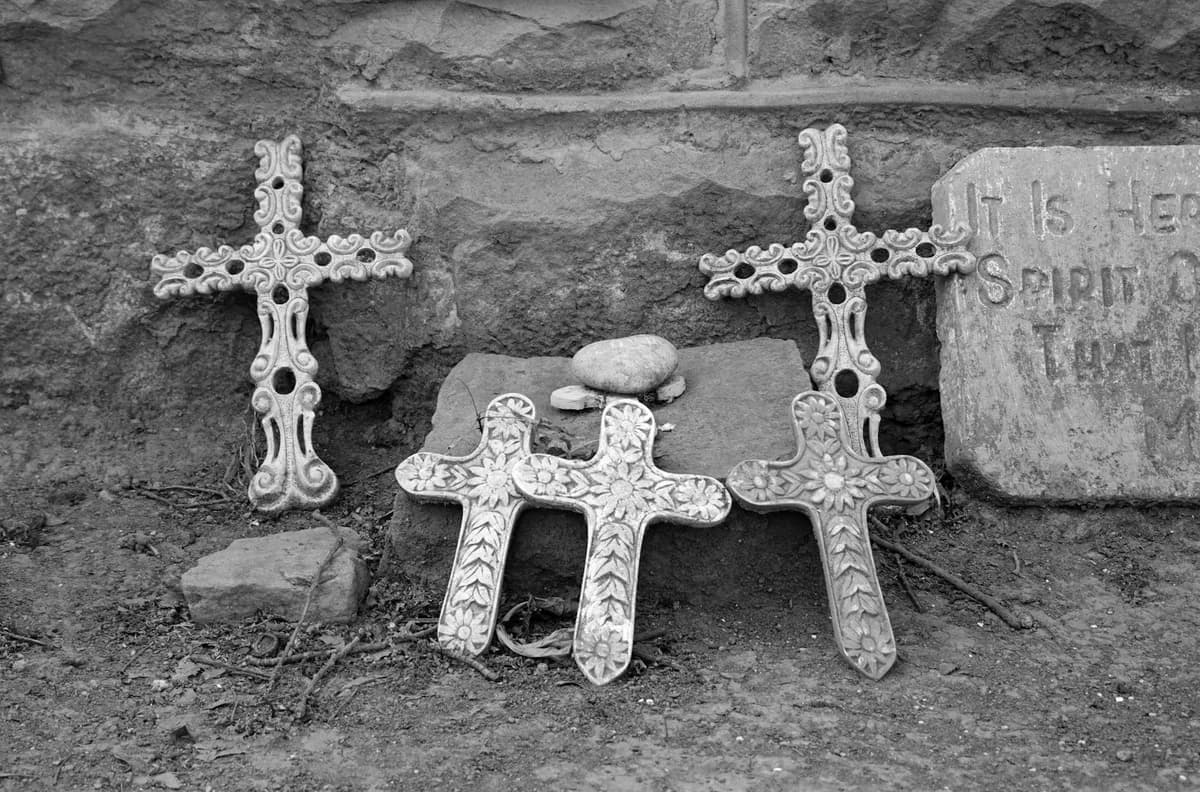 Black and white cemetery scene with intricately designed crosses and a weathered headstone.