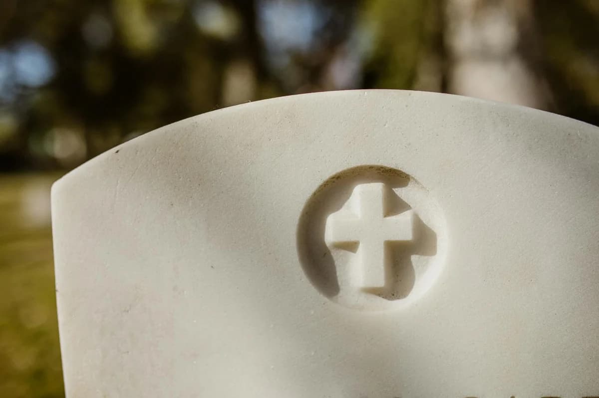 A detailed view of a carved cross on a marble tombstone in a cemetery.