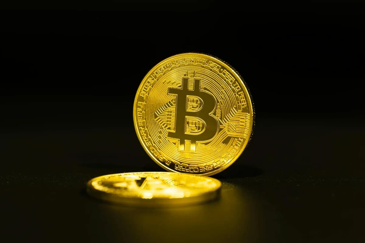Smartphone showing bitcoin price with a physical coin and text representing cryptocurrency investment.