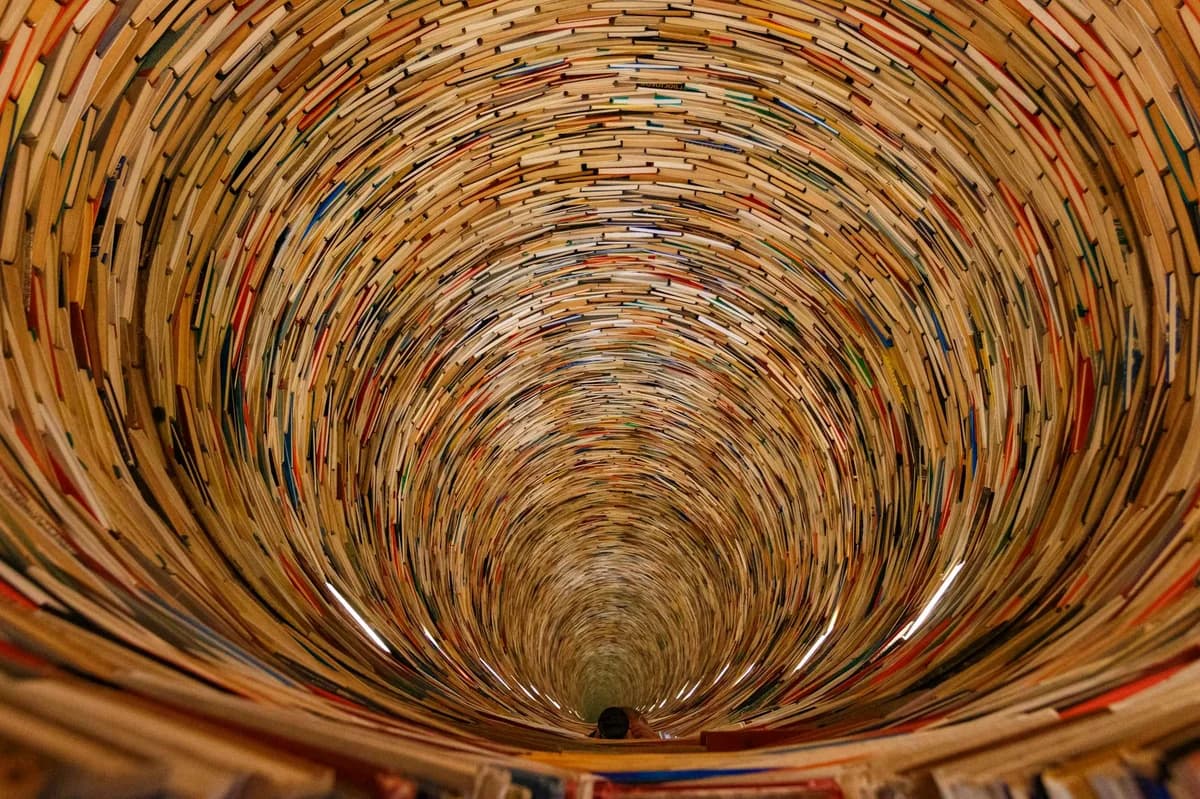 An artistic spiral tunnel made entirely of stacked books creating an intriguing vortex effect.