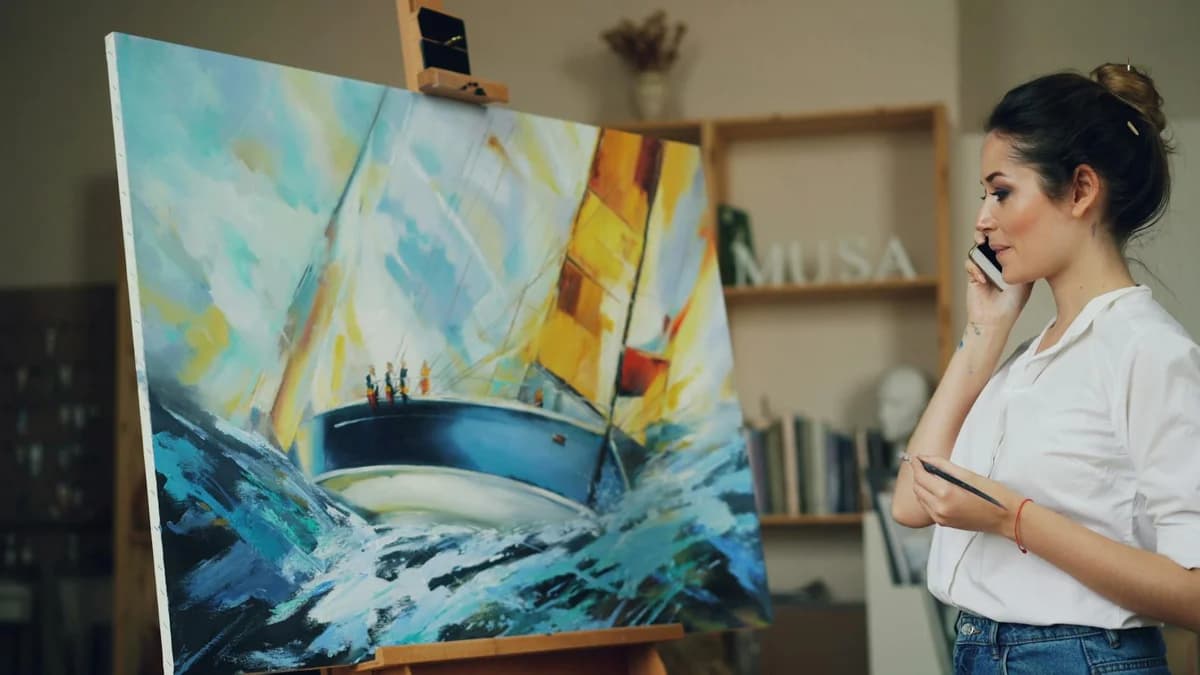 What Is OpenSea and How to Buy NFTs Artist talks on phone while painting a vibrant sailing ship scene on canvas in studio.