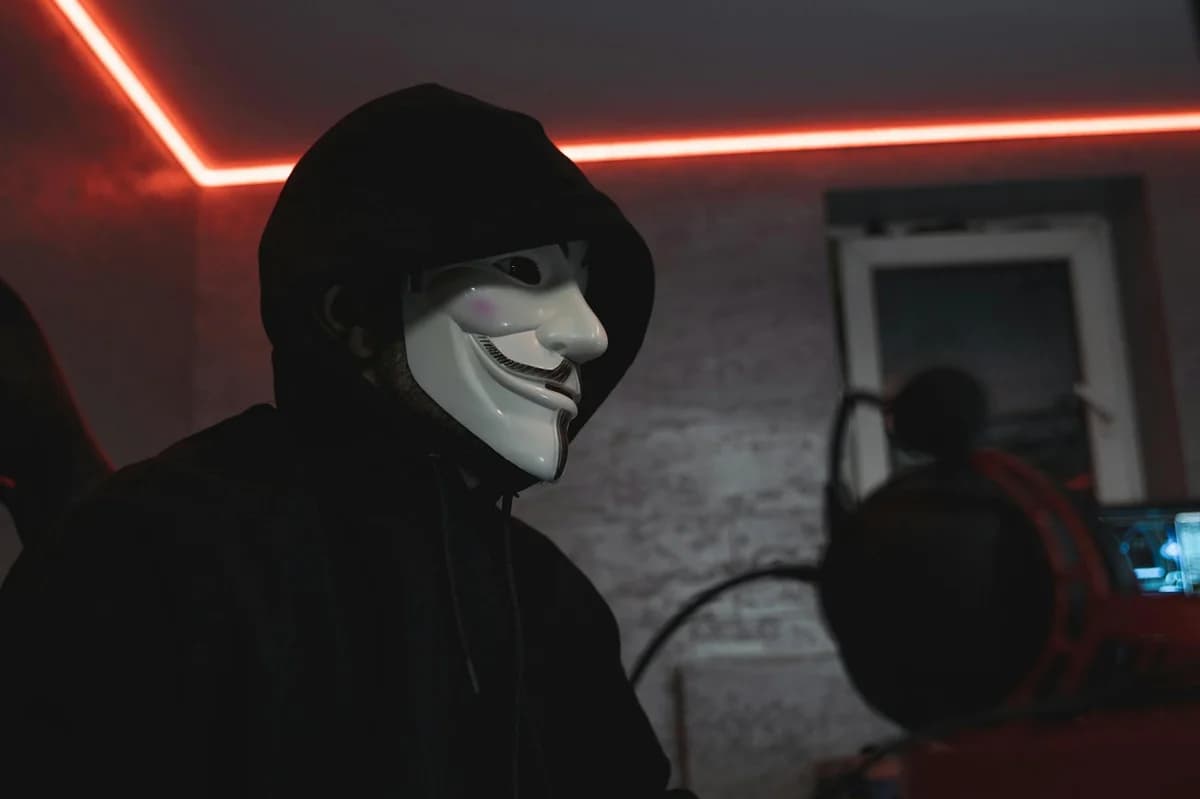 What Is the Biggest DeFi Hack of All Time? Person wearing a hacker mask in a dimly lit room, symbolizing cyber security.